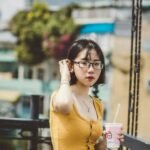 woman in yellow tank top holding white disposable cup